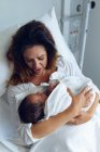 Vista de ángulo alto de la hermosa madre sosteniendo a su bebé recién nacido después del parto en la sala del hospital - foto de stock