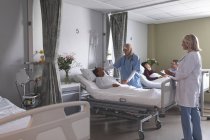 Обзор различных женщин-врачей, взаимодействующих с пациентками смешанной расы в палате больницы. На заднем плане кавказский мужчина держит за руку азиатку, лежащую в постели в больнице . — стоковое фото