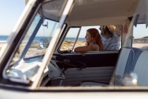 Side view of happy young Caucasian couple looking away near camper van at beach — Stock Photo