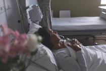 Vista de ángulo alto de la paciente femenina de raza mixta reflexiva que se relaja en la cama en la sala del hospital - foto de stock