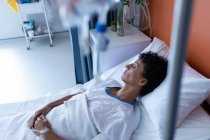 Vue latérale d'une patiente d'âge moyen de race mixte dormant au lit avec les mains sur le ventre dans le service de l'hôpital — Photo de stock