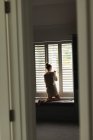 Заднього виду кавказька жінка дивиться через вікно в домашніх умовах — стокове фото