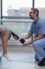 Vue latérale du physiothérapeute masculin caucasien heureux ajustant la jambe prothétique du patient féminin à l'hôpital — Photo de stock