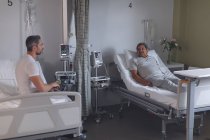 Вид збоку на різних пацієнтів чоловічої статі, що взаємодіють один з одним, розслабляючись на ліжку в лікарні . — стокове фото