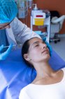 Vista frontal del cirujano varón caucásico de mediana edad inyectando a la cara de una bonita paciente mujer caucásica en el hospital . - foto de stock