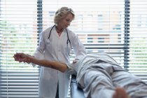Vorderansicht einer kaukasischen Ärztin, die den Arm eines älteren Mischlingspatienten im Krankenhaus untersucht — Stockfoto