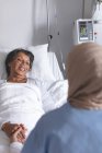 Sopra la spalla vista di razza mista medico femminile in hijab consolante bella paziente di razza mista nel reparto in ospedale. Si stanno tenendo per mano. . — Foto stock
