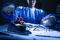 Vue de face du jeune chirurgien mixte tenant des instruments chirurgicaux en salle d'opération à l'hôpital . — Photo de stock