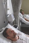 Vue latérale du patient de sexe masculin de race blanche qui dort dans son lit à l'hôpital. En arrière-plan patient masculin mixte âgé couché au lit . — Photo de stock