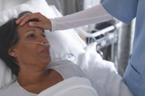 Primer plano de la enfermera de raza mixta comprobando la temperatura de la paciente de raza mixta a mano en la sala del hospital - foto de stock