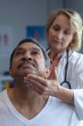 Vue de face du médecin féminin caucasien examinant le cou de patient masculin métis à l'hôpital — Photo de stock