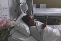 Hochwinkelaufnahme einer schönen Patientin mit gemischter Rasse mittels digitalem Tablet auf der Station im Krankenhaus. — Stockfoto