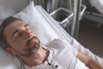 Vista frontal do paciente caucasiano do sexo masculino dormindo na cama na enfermaria do hospital . — Fotografia de Stock