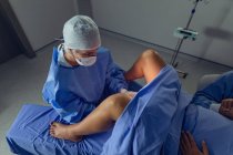Vista de ángulo alto de la cirujana caucásica que examina a la mujer embarazada durante el parto en quirófano en el hospital - foto de stock