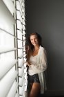 Portrait of Caucasian woman standing near window blind at home — Stock Photo