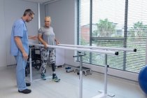 Seitenansicht eines kaukasischen männlichen Physiotherapeuten, der dem Patienten hilft, mit parallelen Gittern im Krankenhaus zu gehen — Stockfoto