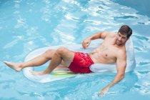 Vista alta do homem caucasiano feliz relaxando em uma melodia inflável na piscina — Fotografia de Stock