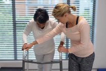 Visão frontal da fisioterapeuta feminina caucasiana ajudando a paciente mestiça a caminhar com andador no hospital — Fotografia de Stock