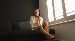 Vista frontale della donna caucasica che utilizza il computer portatile su un divano in soggiorno a casa — Foto stock