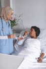 Вид спереду красивий змішаної раси жінка-лікар в Хіджабі дає ліки для зрілої змішаної раси пацієнта в лікарні — стокове фото