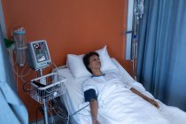 Vue en angle élevé d'une patiente métisse réfléchie couchée au lit dans le service de l'hôpital — Photo de stock