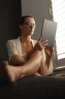 Vista laterale della donna caucasica utilizzando tablet digitale su un divano in soggiorno a casa — Foto stock