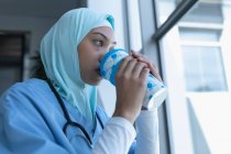 Вид збоку змішаної раси жінка-лікар в хіджабі, яка має каву на сходах в лікарні — стокове фото