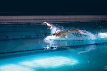 Vista lateral de um nadador caucasiano macho segurando os óculos em sua touca branca enquanto estava na piscina — Fotografia de Stock