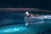 Seitenansicht eines männlichen kaukasischen Schwimmers, der die Brille auf seiner weißen Schwimmmütze hält, während er im Schwimmbad steht — Stockfoto