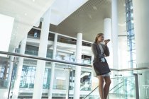 Blick in den niedrigen Winkel: Geschäftsfrau lehnt an Geländer und telefoniert im modernen Bürogebäude — Stockfoto