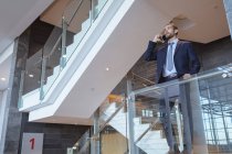 Visão de baixo ângulo do empresário falando no telefone celular perto de trilhos em um prédio de escritórios moderno — Fotografia de Stock