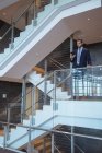 Frontansicht eines Geschäftsmannes, der sein Handy in der Nähe eines Geländers in einem modernen Bürogebäude benutzt — Stockfoto