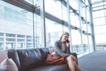 Seitenansicht einer glücklichen Geschäftsfrau, die auf dem Sofa in der Lobby eines modernen Büros mit dem Handy spricht — Stockfoto