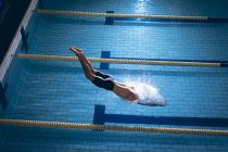 Hochwinkelaufnahme eines männlichen kaukasischen Schwimmers mit weißer Badekappe beim Tauchen im Schwimmbad — Stockfoto