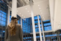 Вид ззаду бізнес-леді, використовуючи гарнітуру віртуальної реальності у вестибюлі в сучасному офісі — стокове фото