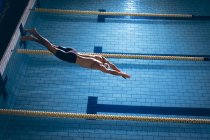 Vista de alto ângulo de um nadador caucasiano masculino que usa um gorro branco mergulhando na piscina — Fotografia de Stock
