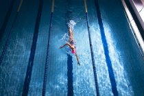 Vista de alto ângulo de uma mulher caucasiana usando um boné de natação rosa e óculos fazendo um golpe estilo livre em uma piscina — Fotografia de Stock