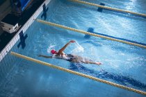 Високий кут зору кавказька жінка в купальнику і рожевий плавальний ковпачок робить Фрістайл інсульту в басейні — стокове фото