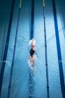 Hochwinkelaufnahme einer kaukasischen Frau mit pinkfarbener Badekappe und Brille, die in einem Schwimmbad einen Rückenschlag macht — Stockfoto
