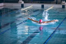 Front view of a Caucasian woman wearing a swimsuit and a pink swimming cap doing butterfly stroke in the swimming pool — Stock Photo
