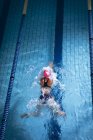Vue en angle élevé d'une femme caucasienne portant un bonnet de bain rose et des lunettes faisant un coup de sein dans une piscine — Photo de stock