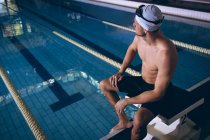 Seitenansicht eines männlichen kaukasischen Schwimmers, der auf einem Sprungbrett am Pool sitzt — Stockfoto
