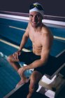 Side view of a male Caucasian swimmer smiling and sitting on a diving board by the swimming pool — Stock Photo