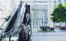 Vista frontal de diversos empresarios que utilizan escaleras mecánicas en oficinas modernas - foto de stock