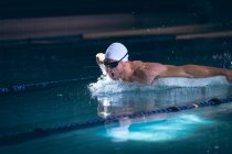 Side view of a male Caucasian swimmer in the goggles and white swimming cap in the swimming pool — Stock Photo