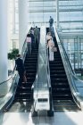 Вид спереди различных бизнесменов, использующих эскалаторы в современном офисе — стоковое фото