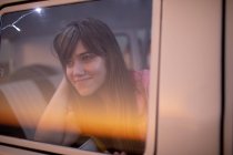 Vista frontal de una hermosa mujer caucásica mirando por la ventana de una caravana en la playa - foto de stock
