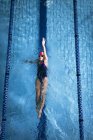 Vue en angle élevé d'une femme caucasienne portant un bonnet de bain rose et des lunettes faisant un coup de dos dans une piscine — Photo de stock