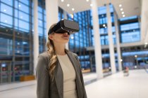 Вид спереду бізнес-леді, використовуючи гарнітуру віртуальної реальності у вестибюлі в сучасному офісі — стокове фото