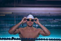 Vorderansicht eines männlichen kaukasischen Schwimmers, der die Brille auf seiner weißen Schwimmmütze hält, während er im Schwimmbad steht — Stockfoto